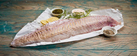 From above closeup of raw pollock fish fillet with fresh dill sprig and lemon slices placed near...