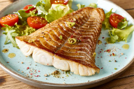 High angle of roasted fish fillet served with vegetables on wooden board on table