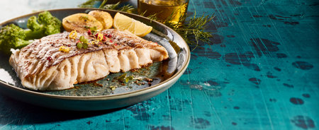 High angle of roasted fish fillet served with vegetables on wooden board on table