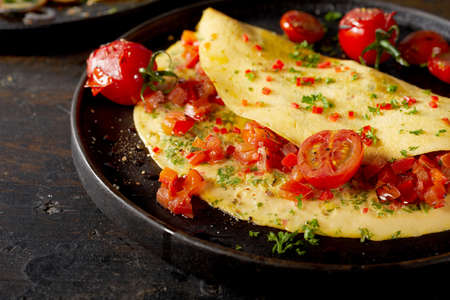 High angle of delicious vegetarian omelette with fresh tomatoes and herbs served on table for lunchの写真素材
