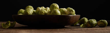 Ripe green Brussels sprout in bowl placed on wooden table on black backgroundの写真素材