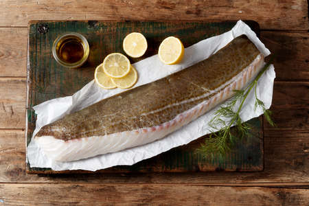Top view composition of fresh uncooked fish fillet placed on paper with lemon slices and olive oil on wooden tableの写真素材