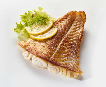 From above appetizing roasted pollack fish arranged on white surface with ripe lemon slices