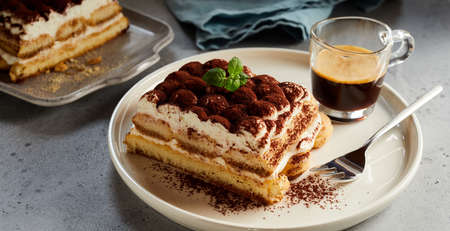 High angle of slice of tasty Tiramisu cake on plate and mug of coffee served on tableの写真素材