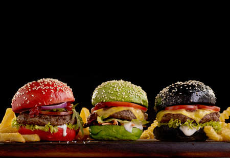 Delicious hamburgers with colorful buns and French fries placed on table on black background in studioの写真素材