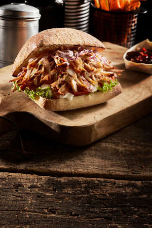 Appetizing pulled pork burger with vegetables served on wooden table in fast food cafe