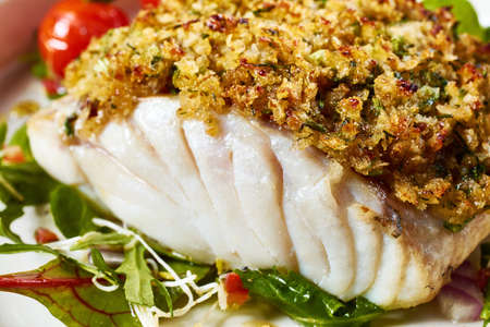 Closeup yummy freshly baked cod fish fillet with coating breadcrumbs served on fresh salad leaves