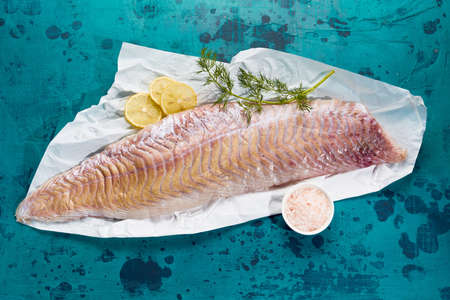 Top view of fresh fish fillet placed on blue background with lemon slices and green dillの写真素材