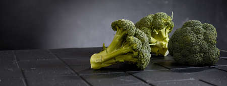 Wide angle of raw broccoli with thick stalks on tiled surface on gray backgroundの写真素材