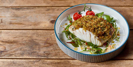 From above tasty cod fish baked with coating breadcrumbs and cherry tomatoes served on plate with...