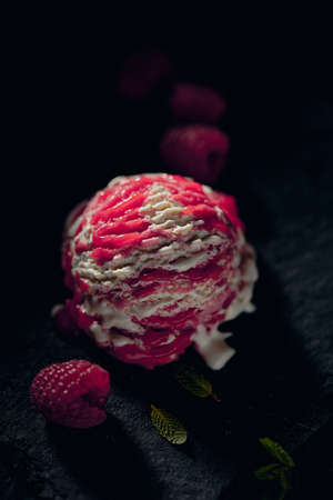 From above of yummy gelato scoop between fresh ripe raspberries and mint leaf on blurred backgroundの写真素材