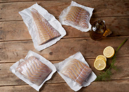 From above of slices of raw fish fillet arranged on wooden table with bottle of olive oil and fresh...