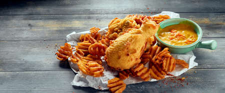 High angle of delicious chicken legs and crispy potato chips on wooden table with sauceの写真素材