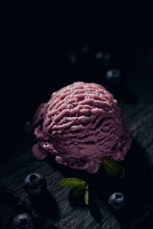 From above of tasty creamy gelato ball between fresh blueberries and mint leaves on dark backgroundの写真素材