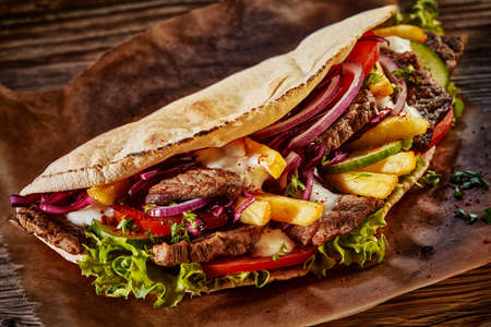 From above of appetizing doner kebab with meat and various fresh vegetables served on wooden tableの写真素材