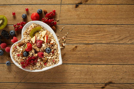 Top view of healthy breakfast bowl with oat and various fresh fruits and berries placed on wooden tableの写真素材