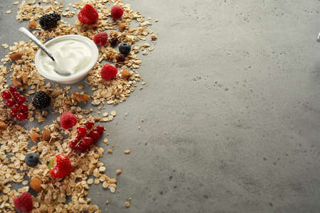 From above of natural yogurt in bowl placed on table with scattered oat and assorted fresh berries