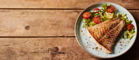 From above of delicious fish fillet served on plate with fresh salad on wooden table