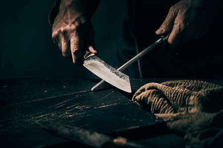 Chef sharpening a large knife on a handheld metal file over an old vintage black chopping board with copyspace in a food preparation conceptの写真素材