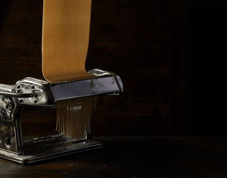 Metal machine with raw pastry for making spaghetti placed on wooden table on black background in studioの写真素材