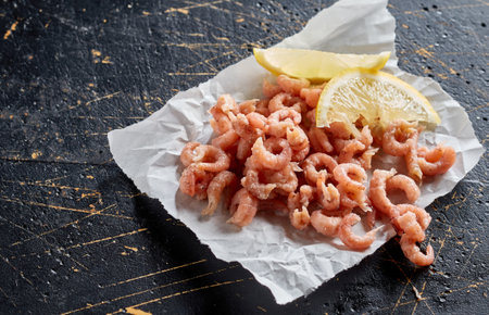 From above of peeled cooked shrimps and fresh lemon slices on baking paper placed on black slate boardの写真素材