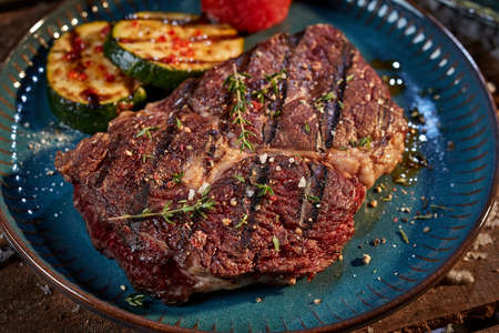 From above of palatable grilled beef steak garnished with herbs and spices served on plate with tomatoes and zucchini on wooden tableの写真素材