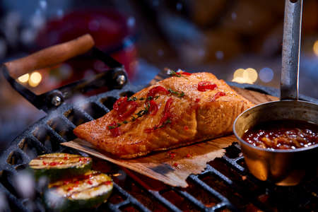 High angle of delicious salmon fillet with seasonings and sauce in bowl being cooked on BBQ gridの写真素材