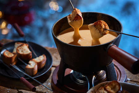 From above of delicious crunchy bread croutons being dipped in hot cheese fondue in pot placed on wooden table in winterの写真素材