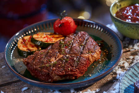 High angle of tasty grilled beef steak and vegetables prepared for winter barbeque placed on plate on wooden tableの写真素材