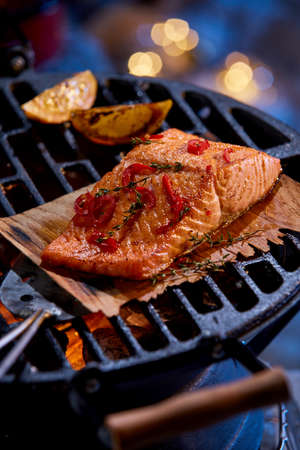 High angle of appetizing piece of salmon fillet with spices being prepared on grill in winter eveningの写真素材