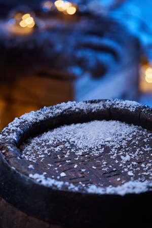 Snow on wooden barrel placed in winter garden with illuminated garland at nightの写真素材