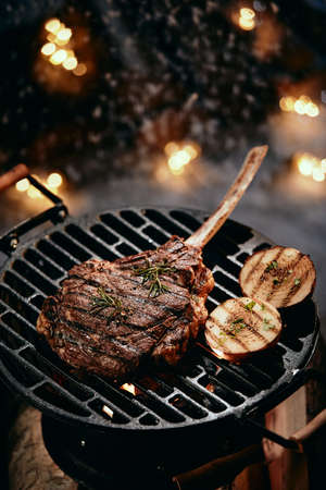 From above of appetizing tomahawk steak with seasonings cooking on round grill against glowing lights in winter timeの写真素材