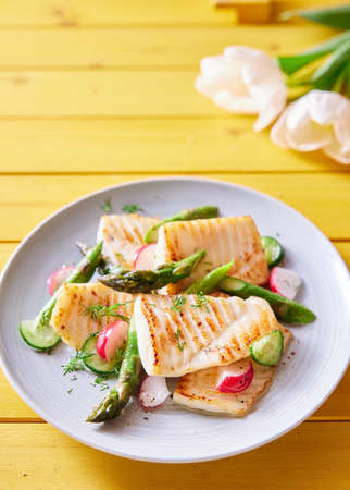 From above of tasty grilled tilapia fish with fresh vegetables served on wooden table with spring...