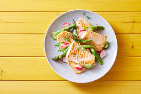 Top view of palatable grilled tilapia fish with cut vegetables served on plate on wooden tableの写真素材