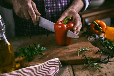 From above of crop unrecognizable man in casual clothes cutting fresh healthy red bell pepper on...