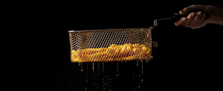 Crop unrecognizable chef holding metal deep fryer basket with French fries and dripping oil against...