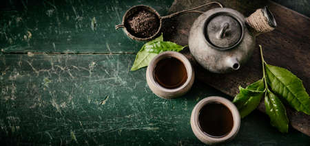Green tea background with ceramic asian teapot and mugs of hot tea with steam on table. Copy space...