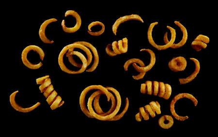Top view of delicious crispy spicy spiral and ring potato fries scattered on black background
