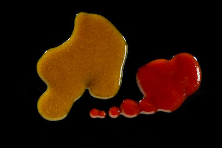 Top view of drops of tomato ketchup and curry sauce on black surface in studioの写真素材