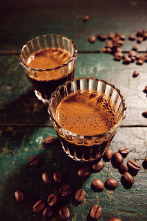 From above of traditional Turkish coffee with froth placed on weathered wooden table with scattered beans in kitchen during breakの写真素材