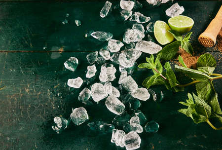 Top view of ingredients for mojito cocktail including heap of ice cubes scattered on shabby table...
