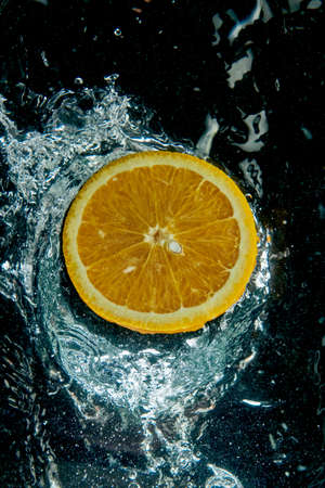 From above round slice of tasty ripe orange on water surface with splashes and water drops in modern...