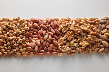 Top view pile of hazelnuts with unpeeled peanuts placed on clear white background with walnuts and...
