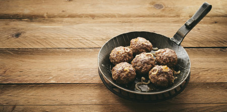 From above rustic metal skillet with fried meat patties and onion placed on wooden table during lunchの写真素材