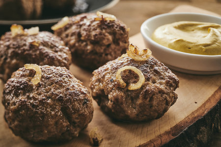 From above closeup traditional German patties with fried onion served on slab near bowl of mustard sauceの写真素材