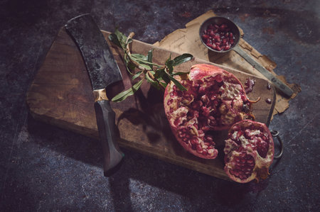 From above of fresh red pomegranate served on wooden chopping board with cleaver knife on gray background with old paperの写真素材