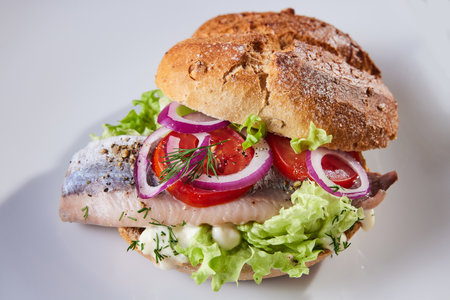Appetizing hamburger with fresh tomatoes and lettuce placed on white plate with fish and onion ringsの写真素材