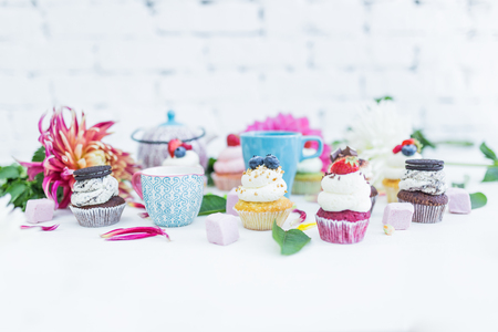 Cupcakes with fresh berries flowers and leaves, a cup of tea or coffee and a kettle.の写真素材