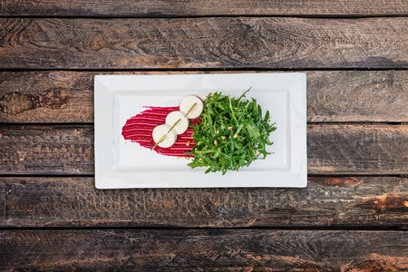 Salad - bakes beetroot slices, goat cheese, fresh arugula and pine nuts, served on the white plate.の写真素材