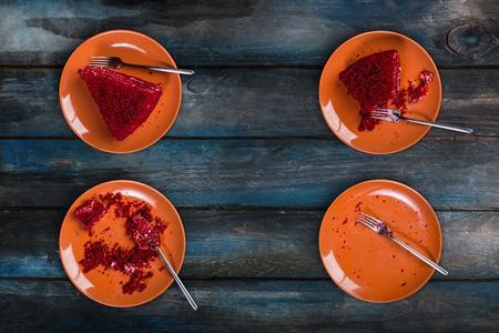 Top View. Eating process of delicious Red velvet cake on a ceramic plate with a fork on a colored wooden backgroundの写真素材